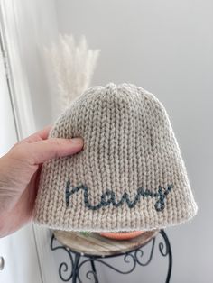 someone is holding up a knitted hat with the word henry written on it in blue ink