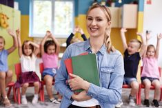 a woman standing in front of a group of children with books on her lap and arms raised