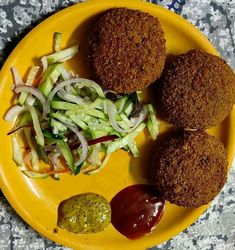 three falafes on a yellow plate with ketchup and salad dressing