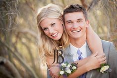 a man and woman hugging each other in front of some trees with their arms around each other