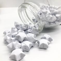 a jar filled with white origami pieces sitting on top of a table next to a pile of smaller ones