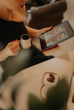 a woman sitting at a table with a tablet and coffee cup in front of her