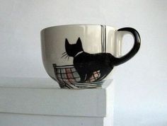 a coffee cup with a black cat on it sitting on top of a stack of books