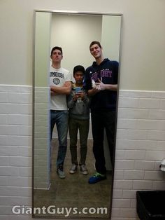 three men standing in front of a bathroom mirror