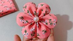 a hand holding a pink flower with white flowers on it and a pearl bead in the center