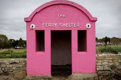 there is a pink sign that says the ferry shelter in front of a stone wall