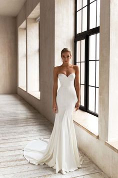 a woman in a white wedding dress standing next to a window