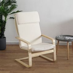 a white chair sitting next to a table on top of a hard wood floor near a potted plant