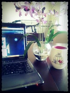 a laptop computer sitting on top of a wooden desk next to a vase with flowers