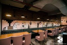 the interior of a restaurant with pink chairs and wall paintings on the walls behind them