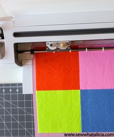 a close up of a machine cutting fabric on a piece of paper with the sewing machine next to it