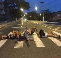 three people laying on the crosswalk at night with their feet up in the air