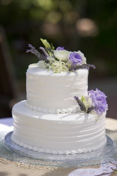 a white wedding cake with purple flowers on top