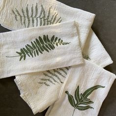 four towels with green leaves on them sitting on a counter top next to each other