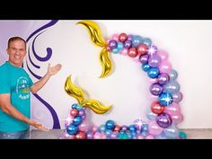 a man standing in front of a balloon arch with mermaid tails on it and balloons all around him