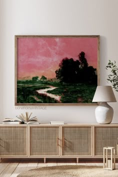 a painting hanging on the wall above a sideboard with a lamp next to it