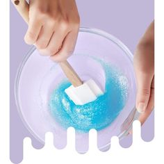 a person using a toothbrush to brush the blue liquid in a bowl with a plastic spoon