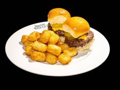 two hamburgers and tater tots on a white plate with black back ground