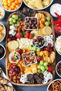 a platter filled with cheese, crackers, fruit and nuts is surrounded by other snacks