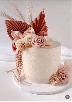 a wedding cake decorated with flowers and feathers on a white tableclothed surface,