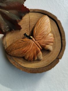 two wooden butterflies sitting on top of a piece of wood in the shape of a leaf