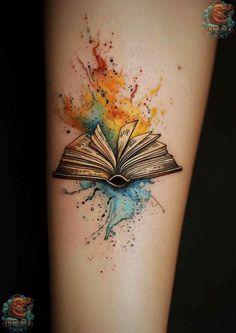 an open book tattoo on the arm with watercolor splashs and paint splatters