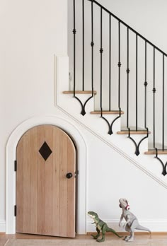 a toy dinosaur is standing in front of a wooden door and staircase with wrought iron handrails