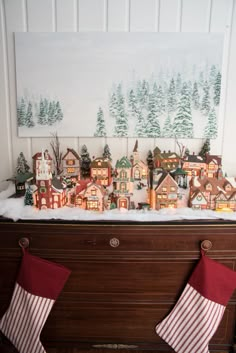 a christmas scene with stockings hanging from the mantle and houses in the background on top of a piano