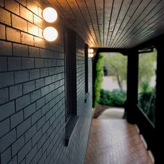 two lights on the side of a brick wall next to a door and walkway with trees in the background