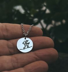 a hand holding a silver necklace with a small black and white drawing on it