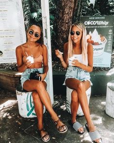 two women sitting next to each other in front of a sign with an ice cream parlour on it