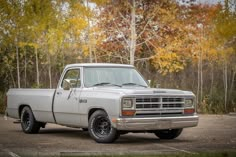 an old pickup truck parked in a parking lot next to trees with yellow and orange leaves