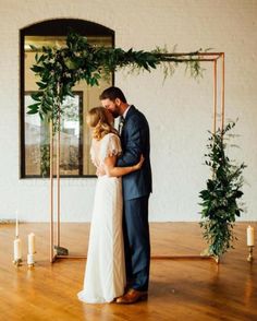 a bride and groom standing in front of a wooden arch with greenery on it