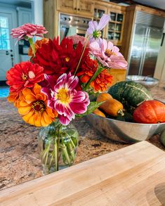 a vase filled with colorful flowers sitting on top of a counter next to fruit and vegetables