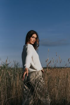 a woman standing in tall grass with her hands on her hips and looking at the camera