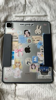 an apple laptop with many stickers on the cover and in front of it is laying on a bed