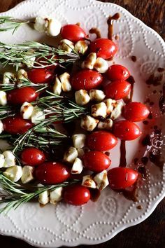 a white plate topped with cherry tomatoes and goat cheese skewered in chocolate sauce