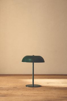 a green table lamp sitting on top of a wooden floor next to a white wall