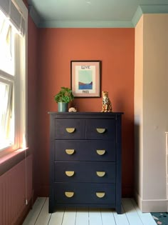 a black dresser with gold handles in a room that has orange walls and white floors