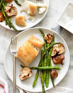 two white plates topped with fish and asparagus on top of a marble table