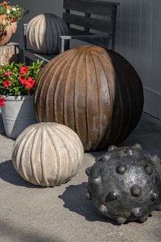 three cement balls sitting next to each other on the ground near potted plants and flowers