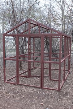 a red metal structure in the middle of a field with trees and bushes behind it