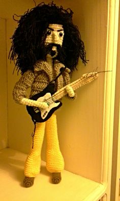 a crocheted stuffed animal plays an electric guitar on a shelf in a room