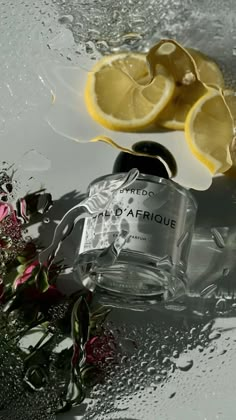 a bottle of perfume sitting on top of a table next to lemons and flowers