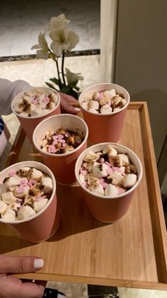 four cups filled with ice cream and toppings on top of a wooden tray next to a flower