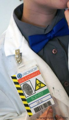 a person wearing a white lab coat and blue bow tie is holding a badge in his hand