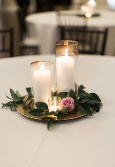 three candles are sitting on a gold plate with greenery and roses in front of them