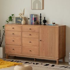 a wooden dresser sitting in a living room next to a rug and potted plant