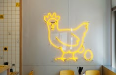 the neon chicken sign is on the wall in the kitchen, next to two yellow chairs