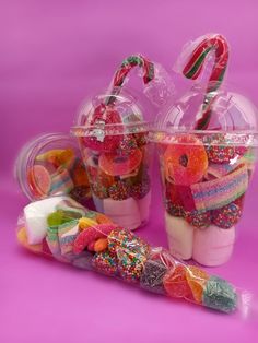 two plastic cups filled with candy and candies on top of a pink background,